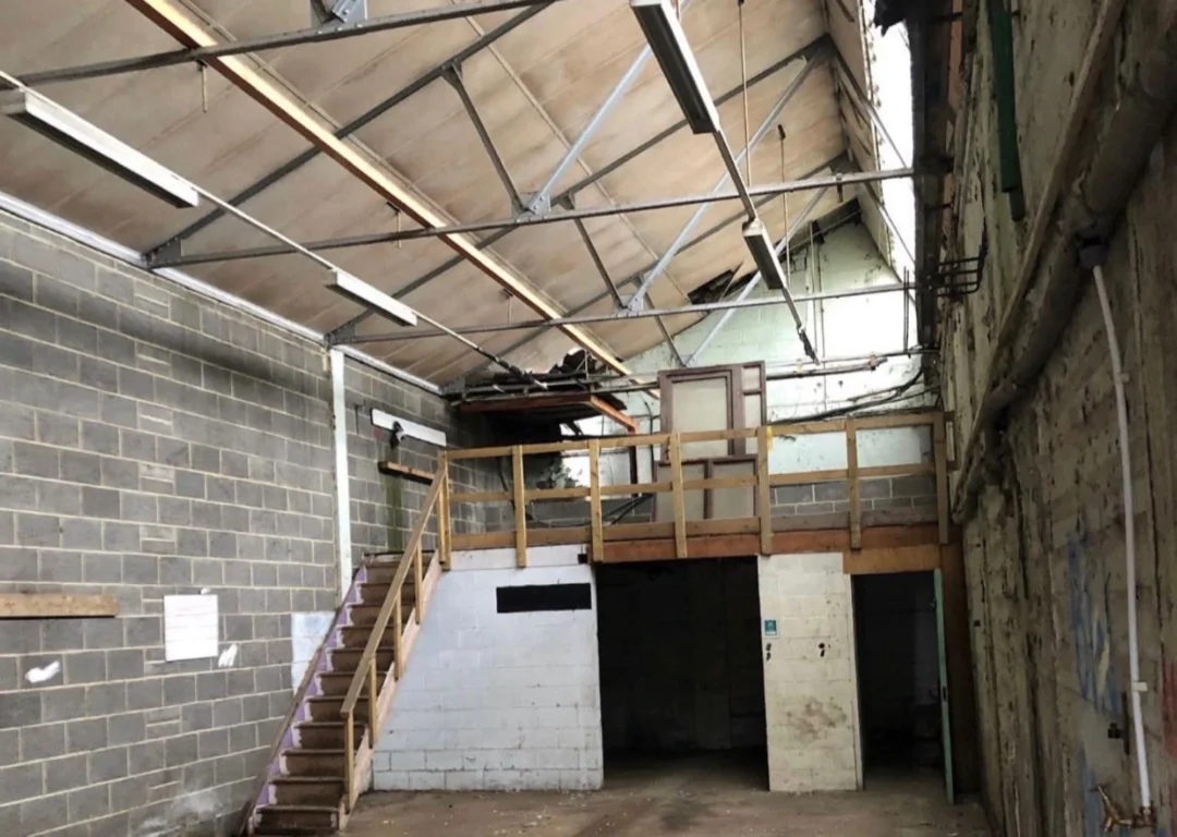 A run down warehouse interior with graffiti and old flooring.
