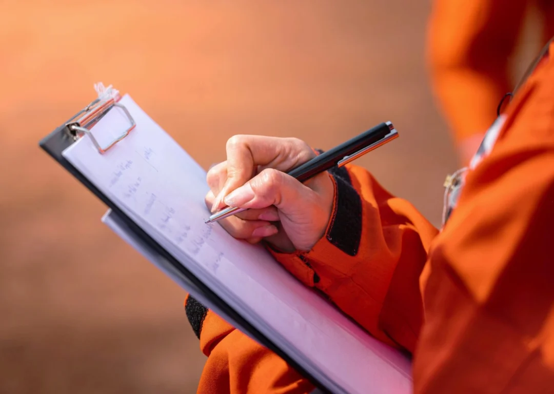 An engineer in orange overalls ticking items off a list on a clipboard.