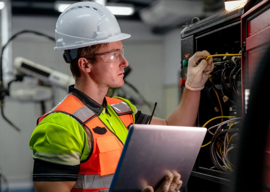 An engineer in an orange hi-vis jacket inspecting wires.
